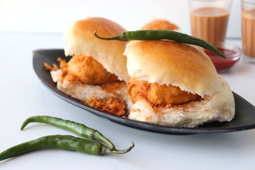 Vada pav or wada pao is a vegetarian fast food dish native to the state of Maharashtra. Famous Mumbai street food served with Red chutney and fried green chili. Copy space