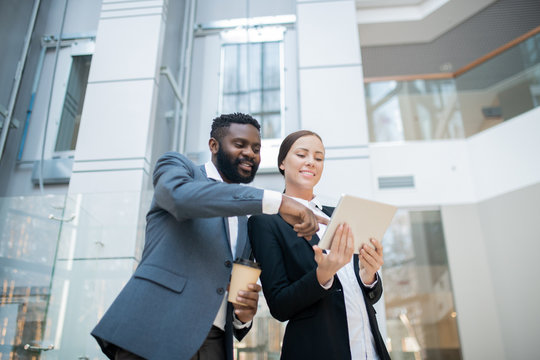 Positive young Black businessman pointing at tablet screen while discussing online project implementation with female colleague