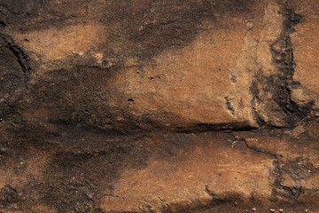 close up of brown stone rock formation texture with black cracks throughout texture background