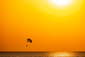 Silhouette of a parachute and a skydiver against the background of a bright burning sunset over the sea. A shining sun and an object flying in the yellow sky.