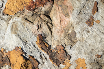 close up of brown, grey, tan and orange sand stone rock formation texture with black cracks throughout texture background