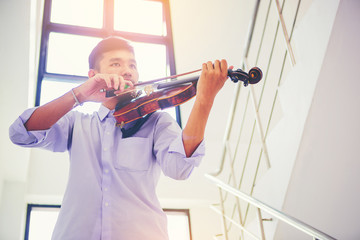 A musician man in white shirt is practicing the violin playing with the melodiousness at stairway. Selected focus.