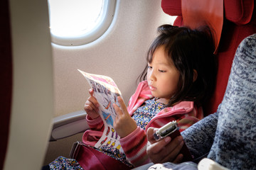 Girl kid is reading Aircraft safety card on flight window seat.