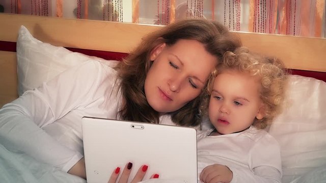 Young woman and adorable little girl using tablet pc sitting on bed
