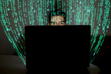 A hacker programmer programs codes on a computer at night. In the foreground is a computer, and...
