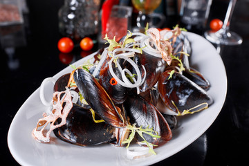 Delicious seafood mussels with arugula and onions. Lemon and baguette . Clams in the shells. Restaurant menu