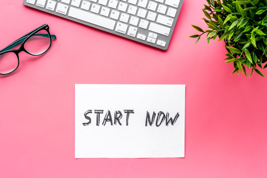 Start now. Motivative text on pink office desk top-down