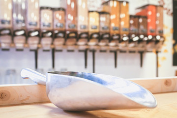 Metal scoop in zero waste shop with bulk dry food dispenser in the background, defocused