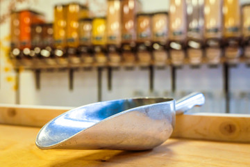 Metal scoop in zero waste shop with bulk dry food dispenser in the background, defocused