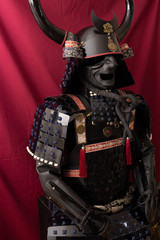 black samurai armor, with scales, with bull horns, exposed in front of a red background