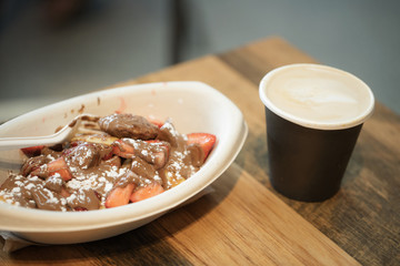 poffertjes pancakes in a paper bowl with strawberries and chocolate with a take away coffee