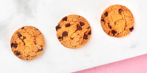 Chocolate chip cookies panorama, shot from above on a white marble and pink background