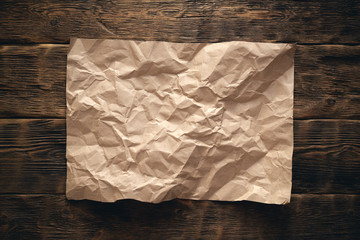 Crumpled blank brown paper page on wooden desk flat lay background.