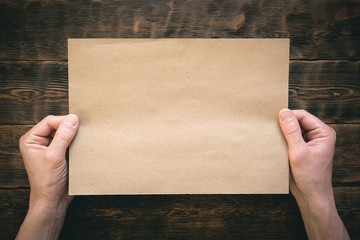Obraz premium Blank brown paper page in male hands on wooden desk flat lay background.