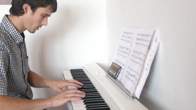 Handsome man tries to play the piano. Young man learns to play the piano with lessons on mobile phone