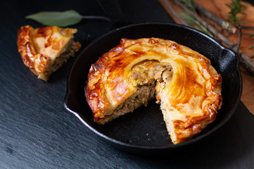 Food concept homemade golden meat puff pastry pie in skillet iron cast on black slate board with copy space