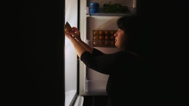 Fat woman opens the fridge at night and takes the cake.Hunger,overeating,diet.