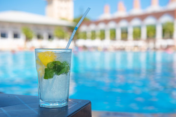 Fresh Mojito Cocktail at the edge of the resort's pool in summer. Luxury vacation concept, a place for text