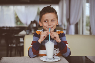 happy smiling little boy in colorful sweater drinking milk shake beverage using straw indoor...