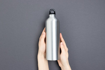Female hands hold metal bottle and mug. Zero waste concept on dark gray background.