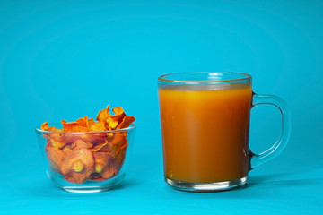 Dried carrot chips in a glass bowl and a glass of carrot juice on a blue background. Organic natural food. Side view, close-up. Pumpkin juice.