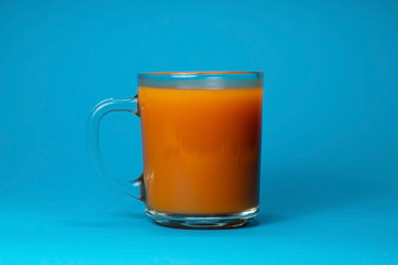 Fresh carrot or pumpkin juice in a glass Cup on a blue background. Close up. Side view. Minimalism. Freshly squeezed vegetable juice.