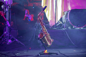 Musical instrument saxophone stands on a stand on the concert stage in the rays of light.