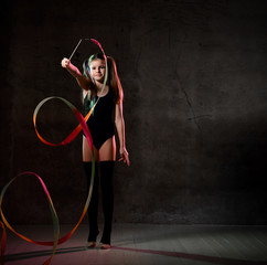 Young smiling girl gymnast in black sport body and uppers standing and making exercise with colorful gymnastic tape