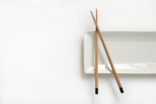 Wooden pairs of chopsticks and ceramic dish on white background. rectangular plate isolated. top view.