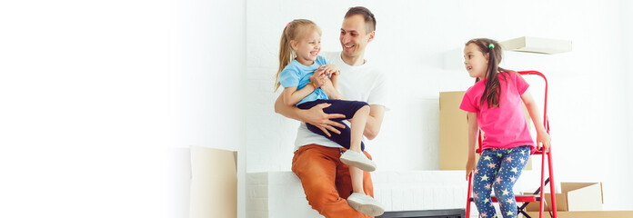 Home repair. Moving young family to new apartment. Repair in house for sale. Happy couple carries small daughter in box at house where repairs are being carried out.