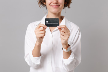 Cropped image of smiling young business woman in white shirt posing isolated on grey background studio portrait. Achievement career wealth business concept. Mock up copy space. Hold credit bank card.