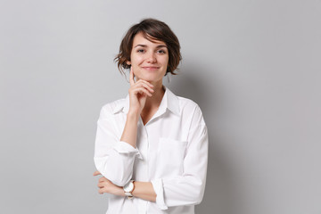 Smiling young business woman in white shirt posing isolated on grey background studio portrait. Achievement career wealth business concept. Mock up copy space. Put hand prop up on chin looking camera.