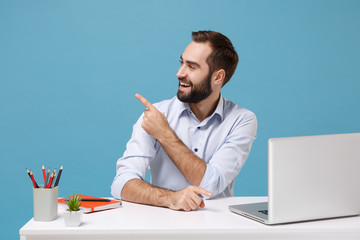 Funny young man in light shirt sit, work at desk with pc laptop isolated on pastel blue background....