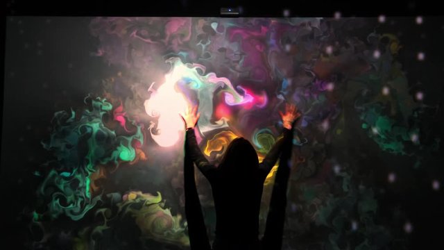 Girl plays with an interactive video installation. New art form, generative graphics. Silhouette of girl draws multi-colored paints interactive installation.