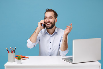 Handsome young bearded man in light shirt sit work at white desk with pc laptop isolated on pastel...