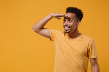 Smiling young african american guy in casual t-shirt posing isolated on yellow orange wall...