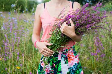Young woman in the field holding a bunch with wild lilac, purple and vilet flowers. 