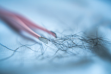 Tweezers and armpit hairs on blue cloth
