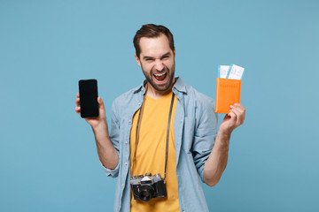 Joyful traveler tourist man in summer clothes with photo camera isolated on blue background. Passenger traveling on weekends. Air flight journey. Hold passport tickets mobile phone with empty screen.