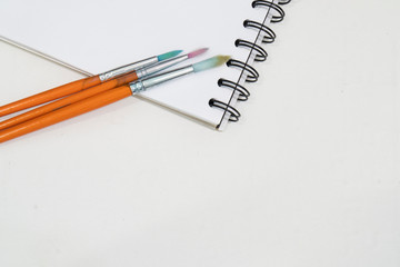 Notebook mock up for artwork with paint brushes. View from above. Artistic work tools on white table.