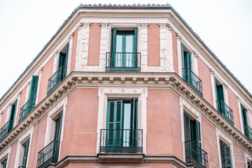 Beautiful pink colored building in downtown Madrid, Spain, with shutters and balconies on windows