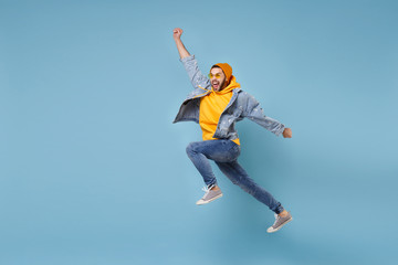 Fototapeta na wymiar Crazy young hipster guy in fashion jeans denim clothes posing isolated on pastel blue background. People lifestyle concept. Mock up copy space. Jumping, spreading hands, clenching fists like winner.