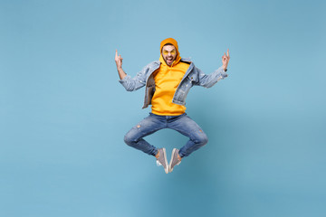 Fototapeta na wymiar Crazy young hipster guy in fashion jeans denim clothes posing isolated on pastel blue wall background studio portrait. People emotions lifestyle concept. Mock up copy space. Jumping showing horns up.