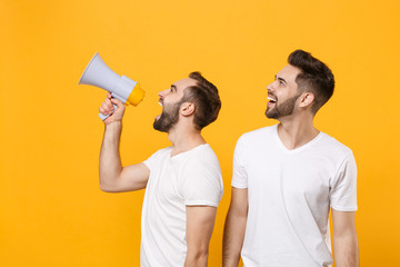 Cheerful young men guys friends in white blank t-shirts isolated on yellow orange wall background studio portrait. People lifestyle concept. Mock up copy space. Scream in megaphone, looking aside.