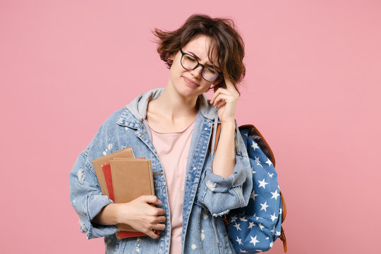 Exhausted young girl student in denim clothes glasses backpack isolated on pastel pink background. Education in high school university college concept. Hold books keeping eyes closed put hand on head.