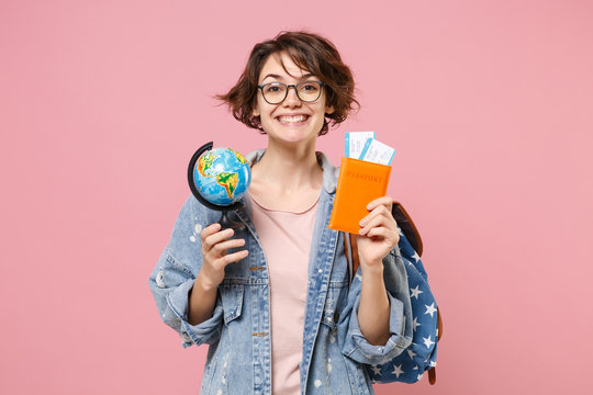 Smiling young woman student in denim clothes eyeglasses, backpack posing isolated on pastel pink background. Education in high school university college concept. Hold passport tickets world globe.