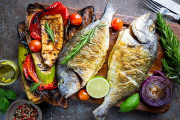 Baked Dorado fish, sea bream with grilled vegetables, herbs and seasonings, top view