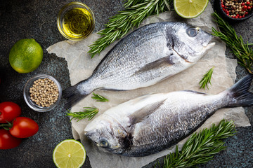Fresh ready to cook raw bream fish dorado with ingredients and seasonings like rosemary, salt, pepper, lime and olive oil, top view