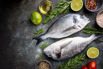 Fresh ready to cook raw bream fish dorado with ingredients and seasonings like rosemary, salt, pepper, lime and olive oil, top view
