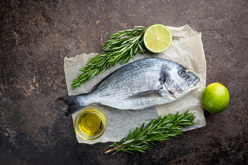 Fresh ready to cook raw bream fish dorado with ingredients and seasonings like rosemary, salt, pepper, lime and olive oil, top view